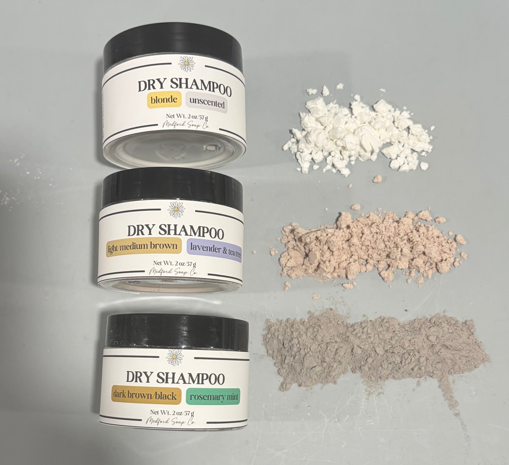 Three containers of dry shampoo with color samples on a gray background