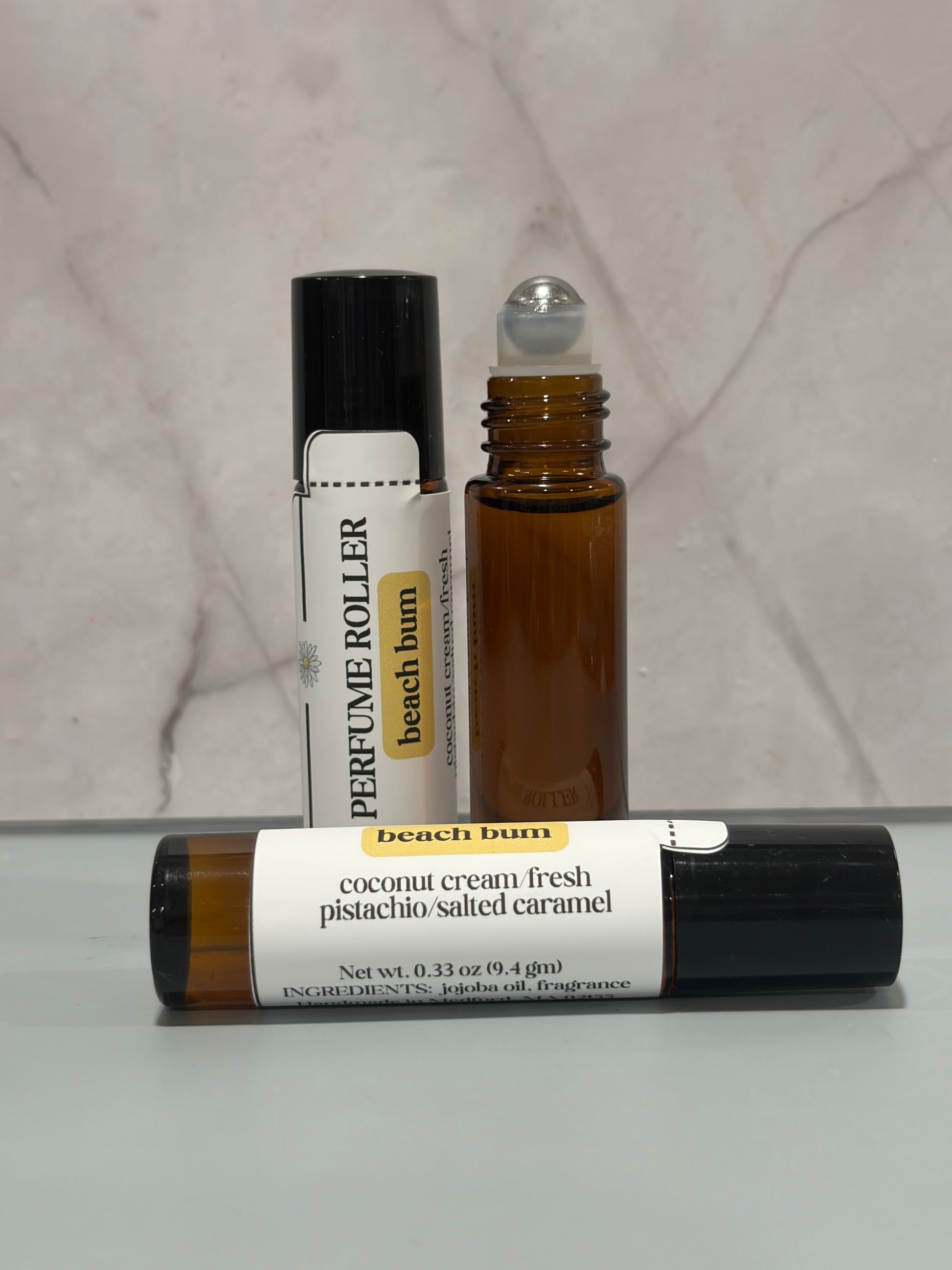 Two rollerball bottles labeled 'beach bum' on a marble surface